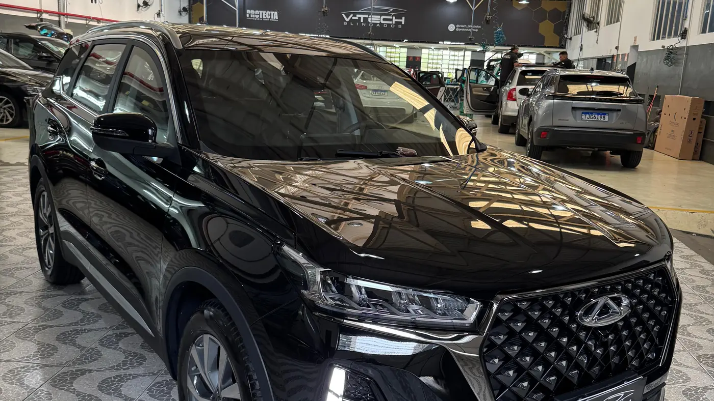 Interior da unidade da V-TECH em São Paulo, com veículos em processo de blindagem e a equipe trabalhando ao fundo